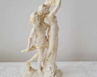 Puede incluir: Una escultura de mármol blanco de una pareja abrazándose. La mujer se está sujetando el pelo y el hombre la está sujetando por la cintura. La escultura está sobre una base blanca con la inscripción "Apollo & Daphne" en la parte delantera.