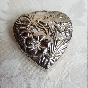 Puede incluir: Una caja de coraz&oacute;n de plata con un dise&ntilde;o floral en relieve.