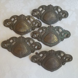 May include: Five antique brass drawer pulls with intricate designs. Each pull features a circular center with a sunburst pattern and a decorative border.