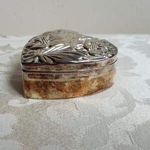 Puede incluir: Una caja de coraz&oacute;n de plata con un dise&ntilde;o floral adornado.