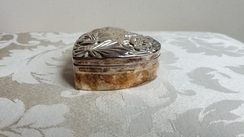 Puede incluir: Una caja de coraz&oacute;n de plata con un dise&ntilde;o floral adornado.