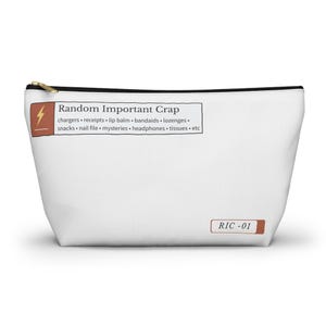May include: White zippered pouch with the text "Random Important Crap" and a list of items. A brown rectangle with a lightning bolt graphic is on the left. The bottom right corner has the text "RIC -01".