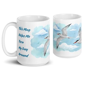 Puede incluir: Taza de cerámica blanca con un diseño de cielo azul y nubes blancas. La taza tiene el texto "This Mug Helps Me Tern My Day Around" impreso en ella. Hay dos pájaros blancos con picos rojos volando en el cielo.