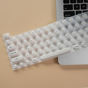 Puede incluir: Cubierta de teclado de silicona blanca con teclas redondas y etiquetas para cada tecla. La cubierta está diseñada para adaptarse a un teclado de computadora portátil estándar.