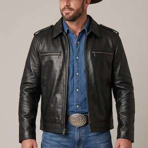 Puede incluir: Chaqueta de cuero negra con camisa vaquera y vaqueros azules, complementada con un sombrero de vaquero marrón. La chaqueta tiene cremallera y dos bolsillos en el pecho. Una hebilla plateada añade un toque western.