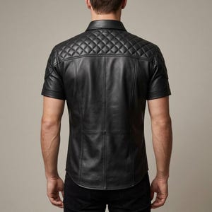 May include: Black leather short-sleeve shirt with a quilted shoulder and upper back design. The shirt has a classic collar and vertical seams down the front and back. The shirt is a solid black color.