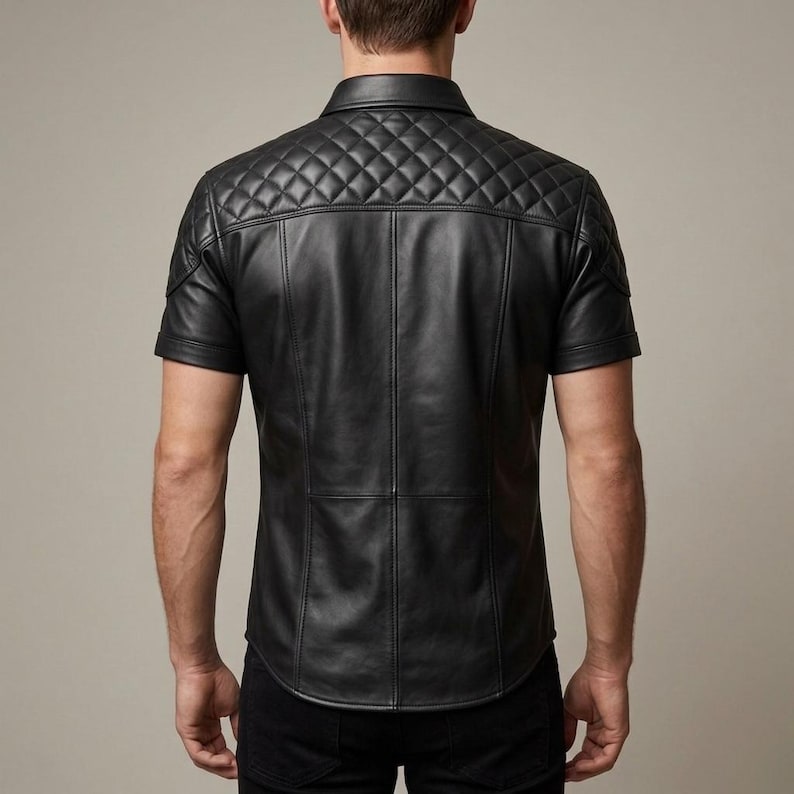 May include: Black leather short-sleeve shirt with a quilted shoulder and upper back design. The shirt has a classic collar and vertical seams down the front and back. The shirt is a solid black color.