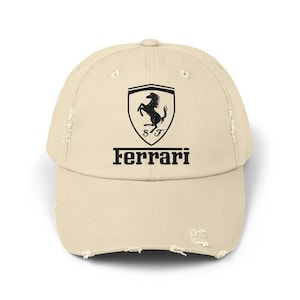 Może przedstawiać: Beżowa czapka z daszkiem z efektem postarzenia, z logo Ferrari. Logo przedstawia czarnego, wspinającego się konia w tarczy, z napisem "Ferrari" w kolorze czarnym poniżej. Czapka ma zużyty, vintage wygląd.