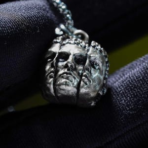 Peut inclure: Un pendentif argenté représentant trois visages divisés verticalement. Le pendentif est suspendu à une chaîne argentée assortie. Les visages présentent des détails précis et une finition légèrement vieillie, créant un look unique et artistique.