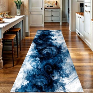 May include: A rectangular runner rug with a blue and white abstract design. The pattern resembles swirling water or clouds, with dark blue accents against a white background. The rug is placed on a wooden floor.