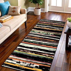May include: A rectangular area rug featuring a horizontal striped pattern composed of black, white, orange, and light green bands. The design incorporates numerous lines of small, printed text resembling record spines or book titles throughout.
