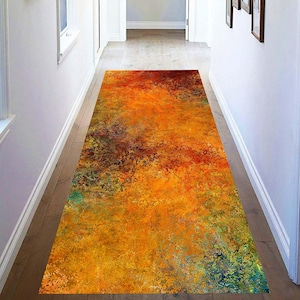 Puede incluir: Una alfombra rectangular para pasillo con un diseño abstracto en tonos naranja, amarillo, rojo y verde. La alfombra está colocada en un pasillo con paredes claras y suelo de madera. El patrón de la alfombra tiene una apariencia texturizada y pictórica.
