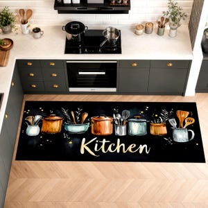 May include: A rectangular kitchen floor mat with a black background featuring a series of illustrated copper and silver pots, pans, and cooking utensils. The word Kitchen is written in a large, elegant gold script font across the center.
