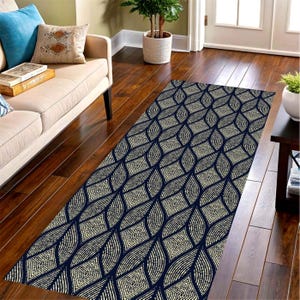 May include: A rectangular rug with a repeating pattern of cream-colored geometric shapes on a navy blue background. The rug is placed on a hardwood floor, with a sofa and decorative pillows visible in the background. The rug's design adds a touch of elegance to the room.