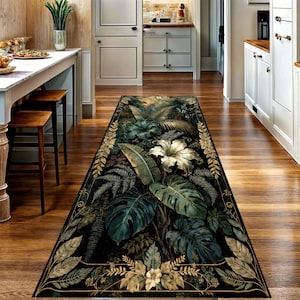 May include: A rectangular runner rug featuring a dark background with a botanical pattern of large green monstera leaves, ferns, and white hibiscus flowers. The design is framed by a decorative border of golden-toned leaves and vines.