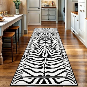 Peut inclure: Un long tapis rectangulaire à imprimé zébré en noir et blanc. Le tapis présente un motif audacieux de rayures noires sur fond blanc, avec une bordure noire. Le tapis est posé sur un parquet dans un couloir.