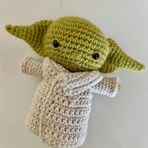 Puede incluir: Mu&ntilde;eca de ganchillo hecha a mano que se asemeja a un personaje popular. La mu&ntilde;eca tiene una cabeza verde con orejas grandes, ojos negros y mejillas rosadas. Lleva una t&uacute;nica de color beige. La mu&ntilde;eca est&aacute; hecha con un punto de ganchillo apretado.
