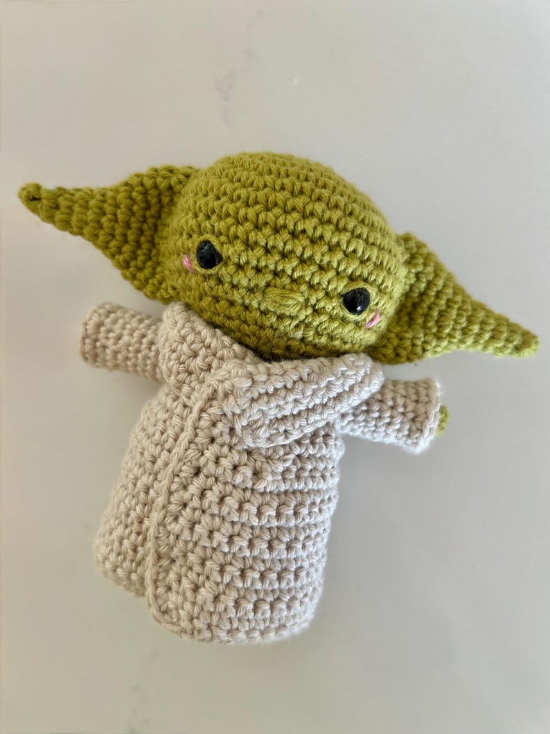 Puede incluir: Mu&ntilde;eca de ganchillo hecha a mano que se asemeja a un personaje popular. La mu&ntilde;eca tiene una cabeza verde con orejas grandes, ojos negros y mejillas rosadas. Lleva una t&uacute;nica de color beige. La mu&ntilde;eca est&aacute; hecha con un punto de ganchillo apretado.