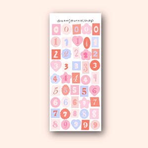 Könnte beinhalten: Ein Stickerbogen mit den Zahlen 0-9 in verschiedenen Formen und Farben. Die Aufkleber sind in Rosa-, Pfirsich- und Blautönen gehalten und haben eine handschriftliche Schriftart. Der Text "dreamjournalshop" steht oben.