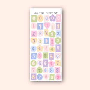 Könnte beinhalten: Ein Stickerbogen mit den Zahlen 0-9 in Pastellfarben. Jede Zahl hat eine andere Form und Farbe, darunter Rosa, Blau, Grün und Gelb. Der Text "dreamjournalshop" steht oben.