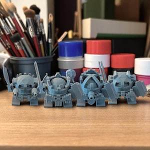 May include: Four gray, 3D-printed robot figurines with various weapons and shields. Each robot has a unique design, with details like swords, maces, and shield-like structures. The figurines are displayed on a wooden surface.