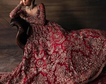 May include: A red formal gown with intricate gold embroidery and long sleeves. The dress features a deep V-neckline and a flowing skirt, creating an elegant silhouette. The gown is embellished with detailed patterns and textures, perfect for special occasions.