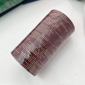 Op de afbeelding: Een bundel bordeauxrode armbanden met een gouden stippenpatroon, verpakt in doorzichtig plastic. De armbanden zijn op elkaar gestapeld, waardoor een cilindrische vorm ontstaat. De achtergrond is wit.