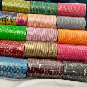 Op de afbeelding: Een verzameling kleurrijke armbanden in verschillende tinten, waaronder groen, roze, oranje en blauw. Elke armband is versierd met een delicaat stippenpatroon. De armbanden zijn netjes gerangschikt en tonen een verscheidenheid aan kleuren en ontwerpen.