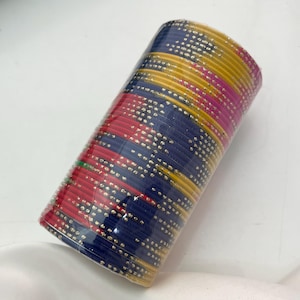 Op de afbeelding: Een bundel kleurrijke armbanden verpakt in doorzichtig plastic. De armbanden zijn in tinten rood, blauw, geel en roze, met een stippenpatroon. De armbanden zijn op elkaar gestapeld, waardoor een cilindrische vorm ontstaat.