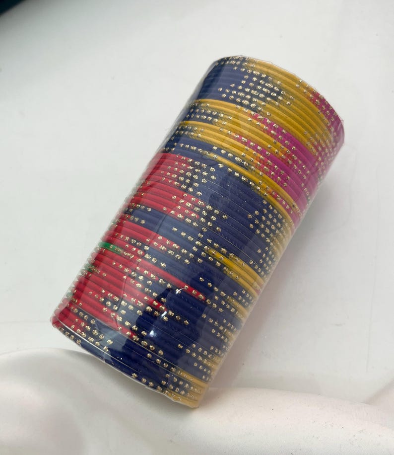 Op de afbeelding: Een bundel kleurrijke armbanden verpakt in doorzichtig plastic. De armbanden zijn in tinten rood, blauw, geel en roze, met een stippenpatroon. De armbanden zijn op elkaar gestapeld, waardoor een cilindrische vorm ontstaat.