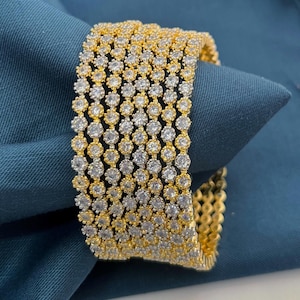 Peut inclure: Un ensemble de cinq bracelets joncs dorés, chacun orné d'une rangée continue de petites pierres rondes et transparentes serties en motif circulaire. Les bracelets présentent une finition jaune métallique et une surface réfléchissante.