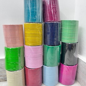 May include: A collection of thin metal bangles arranged in fourteen separate stacks, each wrapped in clear plastic. The stacks feature a variety of solid colors including teal, magenta, light pink, yellow, navy blue, lime green, black, and light blue.