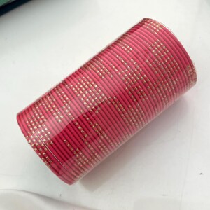 Op de afbeelding: Een stapel roze armbanden met gouden accenten. De armbanden zijn verpakt in doorzichtig plastic. De gouden accenten zijn kleine, gelijkmatig verdeelde stippen. De armbanden zijn een levendige roze kleur.