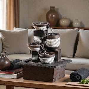 以下が含まれることがあります： 素朴な茶色の仕上げの、多層の屋内噴水。 噴水は、水が流れ落ちる複数のボウルを備えています。 ボウルは白と茶色のストライプのデザインです。 噴水は木製のテーブルの上に置かれています。