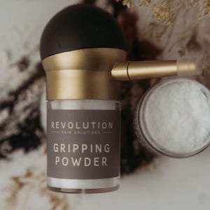May include: A hair care product set featuring a dark brown and gold gripping powder applicator and a small jar of white powder. The applicator has the text "REVOLUTION HAIR SOLUTIONS GRIPPING POWDER" on the label.