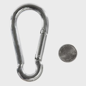 May include: A silver-colored carabiner clip with a spring-loaded gate, next to a U.S. quarter coin. The carabiner is a metal loop with a hinged section that opens and closes. The quarter coin is silver and shows the profile of George Washington.