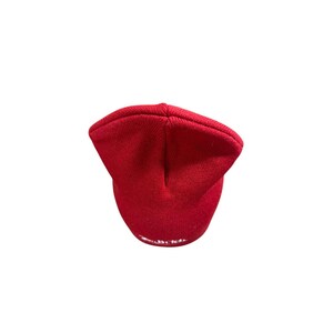 Puede incluir: Un gorro de punto de color rojo brillante con un dobladillo plegado en el borde inferior. El tejido presenta una textura acanalada consistente en toda la superficie del gorro. Un peque&ntilde;o detalle de texto bordado en blanco es visible en el dobladillo.