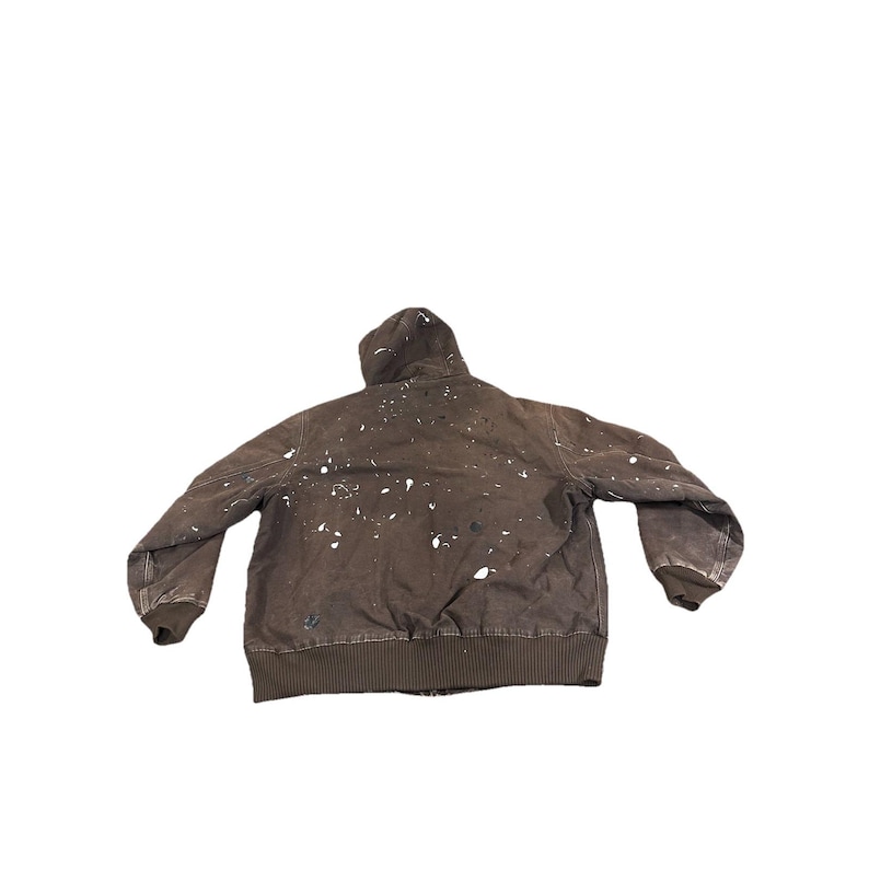 May include: Brown hooded jacket with white paint splatters. The jacket has a ribbed hem and cuffs. The jacket is a workwear style.