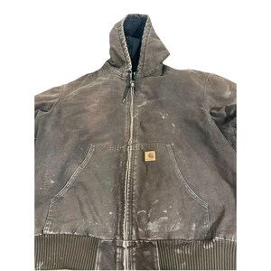 May include: A brown hooded zip-up jacket with a black interior lining. The jacket has a front pocket and a small logo patch. The jacket shows signs of wear with paint splatters and a ribbed hem.