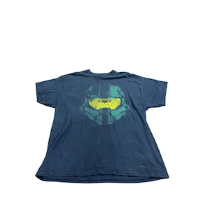 Op de afbeelding: Donkerblauwe t-shirt met een groen en geel helm-afbeelding. De afbeelding is een gestileerde weergave van een futuristische helm. Het shirt is gemaakt van zacht materiaal.