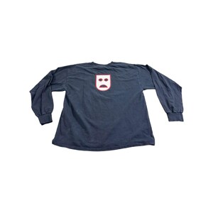 May include: A dark navy blue long-sleeve shirt. The shirt features a white and red graphic on the back, depicting a stylized face. The shirt has a crew neck and long sleeves with ribbed cuffs. The shirt is made of a soft, comfortable material.