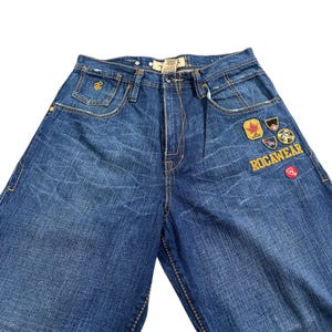 Calça jeans vintage Rocawear Y2K com patches, estilo baggy hip hop, cor índigo, pernas largas e bordados.