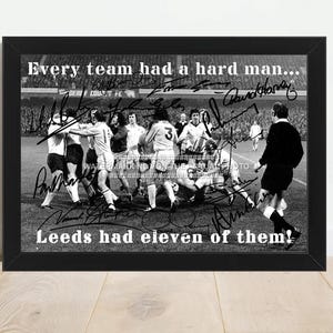 May include: Framed black and white print depicting a soccer match with players in action. The print includes the text "Every team had a hard man... Leeds had eleven of them!" and various signatures.
