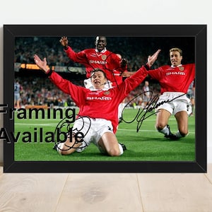 May include: Framed photograph of three footballers in red shirts and white shorts celebrating on a green pitch. The image includes autographs and the text "Framing Available" in the lower left corner.