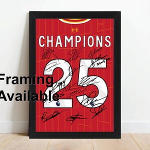 May include: A framed print of a red football shirt with the number 25 in white. The shirt has the word "CHAMPIONS" printed on it and is signed by multiple players.
