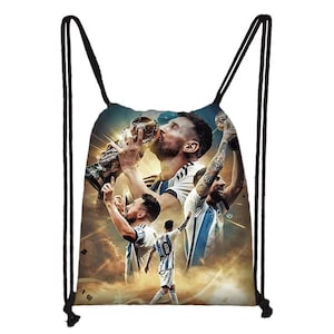 Peut inclure: Sac de sport blanc et bleu avec un collage d'un joueur de football embrassant un trophée et célébrant. Le fond a une teinte dorée nuageuse et le sac a des cordons noirs.
