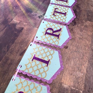 Puede incluir: Una pancarta de cumplea&ntilde;os azul claro y morada con escamas doradas brillantes y la palabra "BIRTHDAY" en letras moradas.