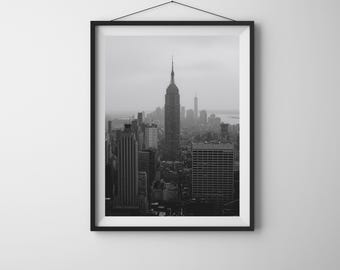 Könnte beinhalten: Schwarz-Weiß-Druck mit Rahmen des New Yorker Stadtbildes, mit dem Empire State Building im Mittelpunkt. Das Bild zeigt die berühmte Architektur und den Stadtlandschaft, präsentiert in Graustufen.