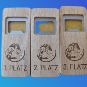 Puede incluir: Tres abridores de botellas de madera con inserciones metálicas. Cada abridor tiene una clasificación diferente: 1. PLATZ, 2. PLATZ y 3. PLATZ. Los abridores presentan un gráfico circular de una persona pescando.