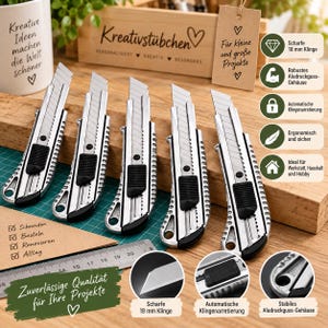 Könnte beinhalten: Fünf silberfarbene Cuttermesser mit schwarzen Schiebemechanismen und einziehbaren Klingen, in einer Reihe auf einer Holzoberfläche angeordnet, neben einem Metalllineal mit Zentimeter-Skala und einem Anhänger mit deutschem Text.